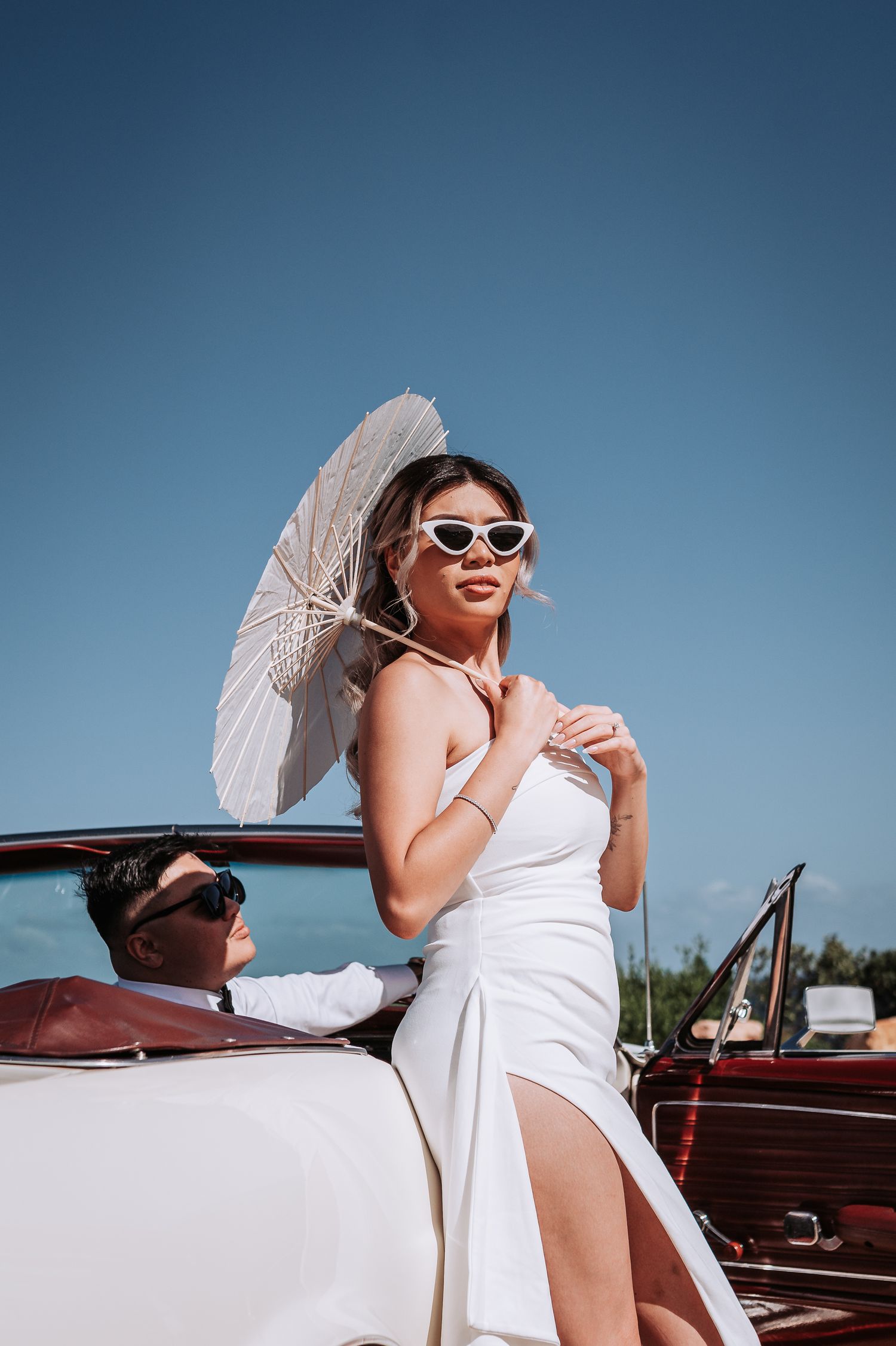 A retro-inspired scene with a white parasol and vintage car by the ocean.