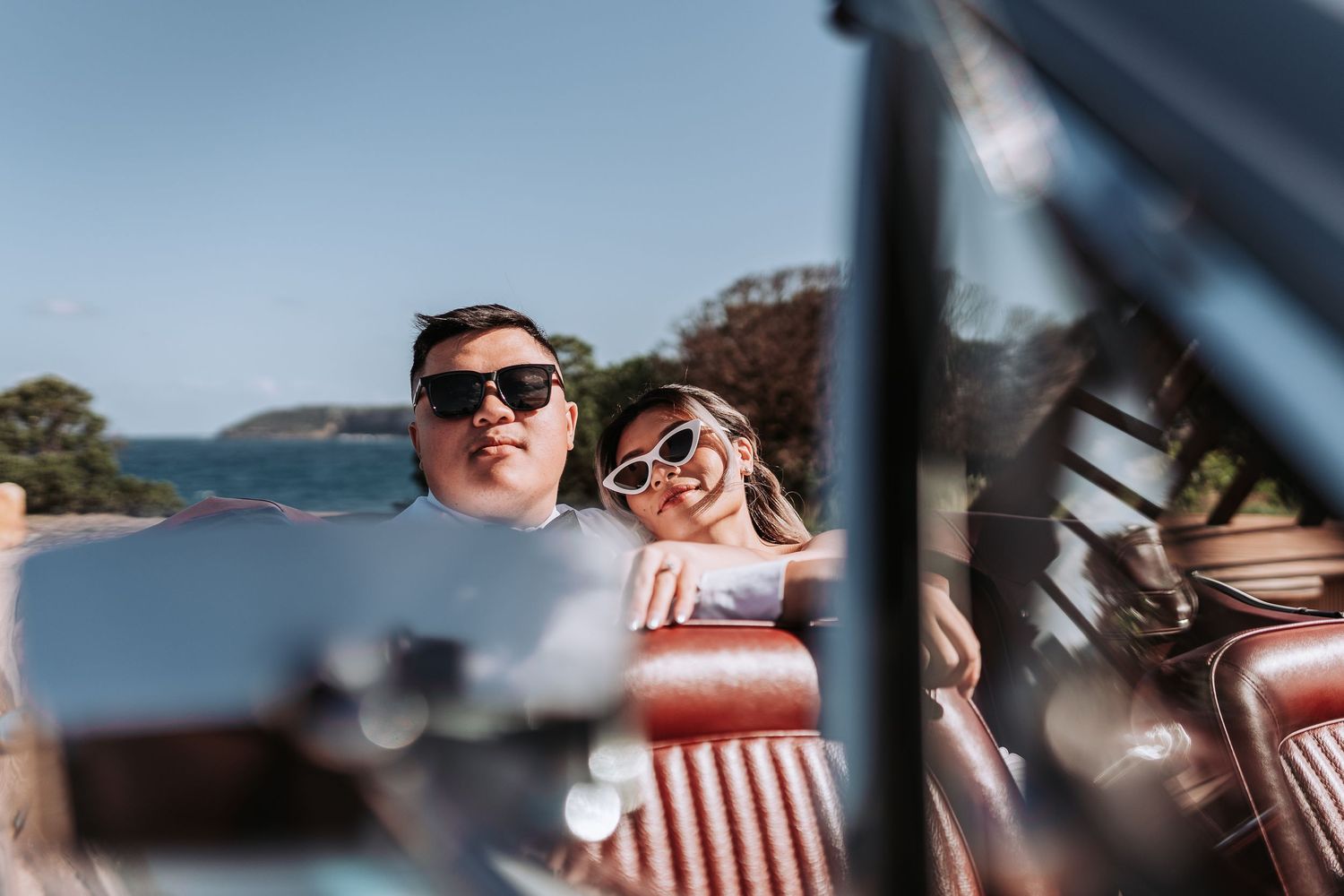 Joyful couple in sunglasses reflected in the mirror of a vintage convertible car.
