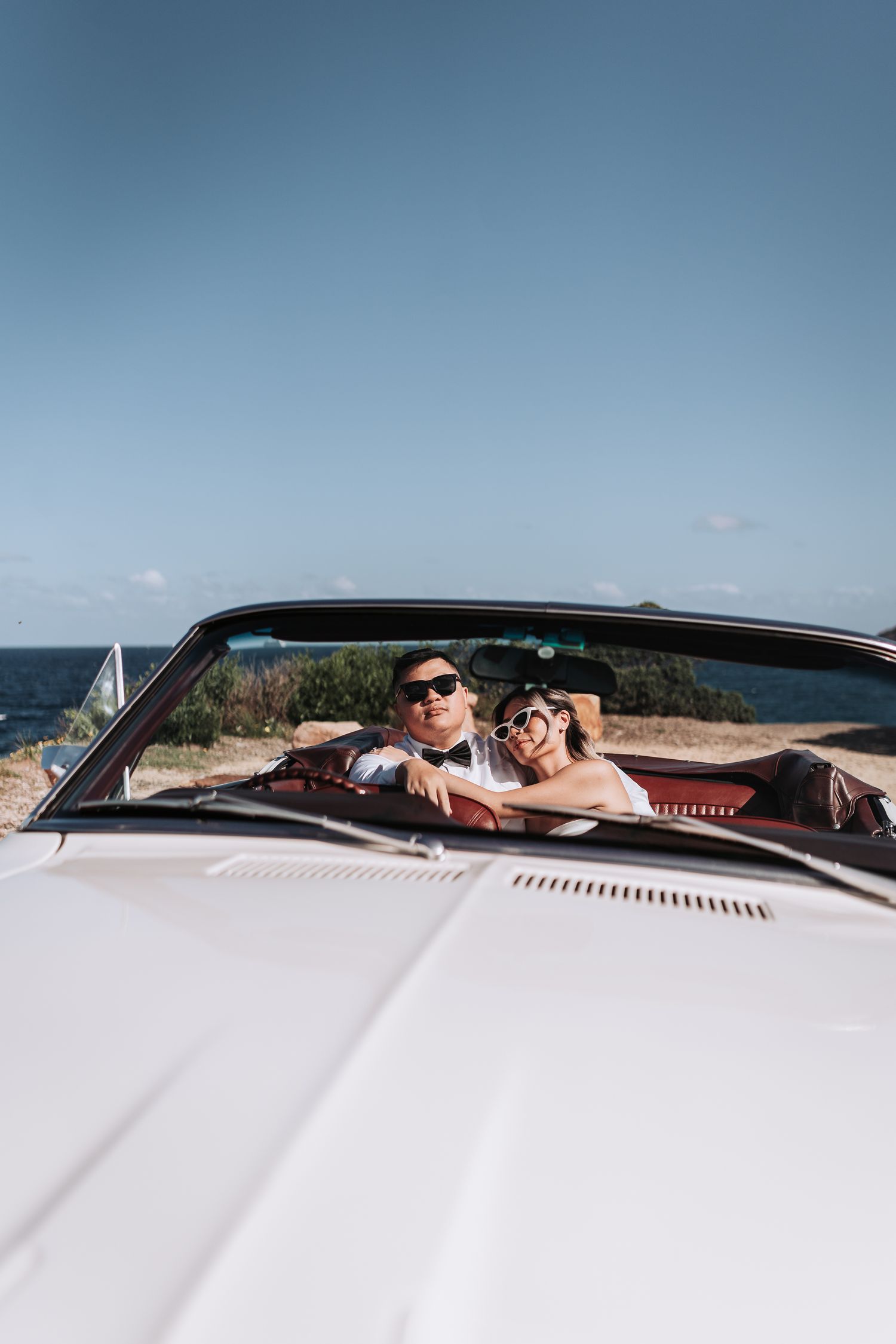 Stylish couple in a white classic convertible car overlooking the ocean.
