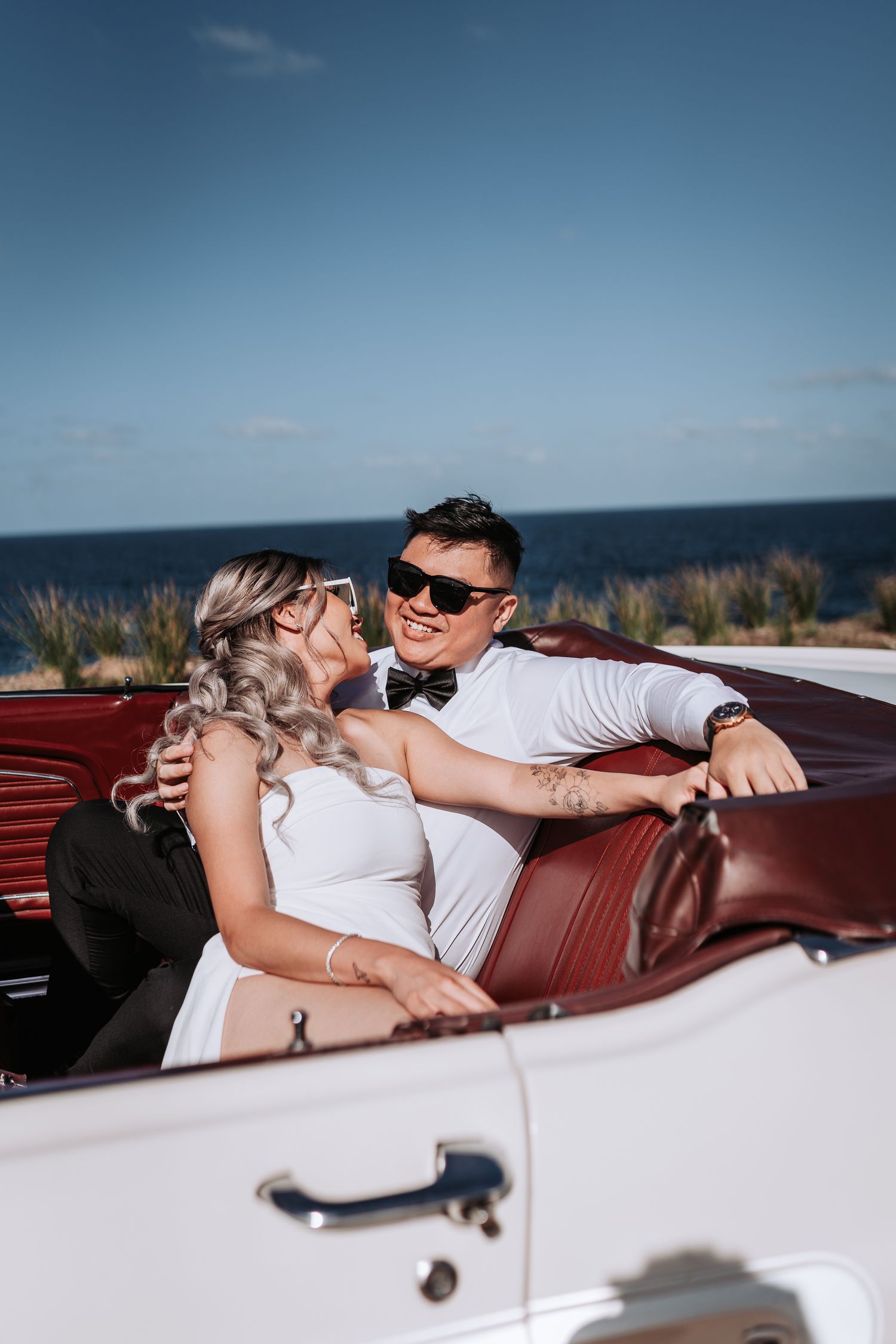 Romantic moment shared between newlyweds in a vintage white convertible with red interior.