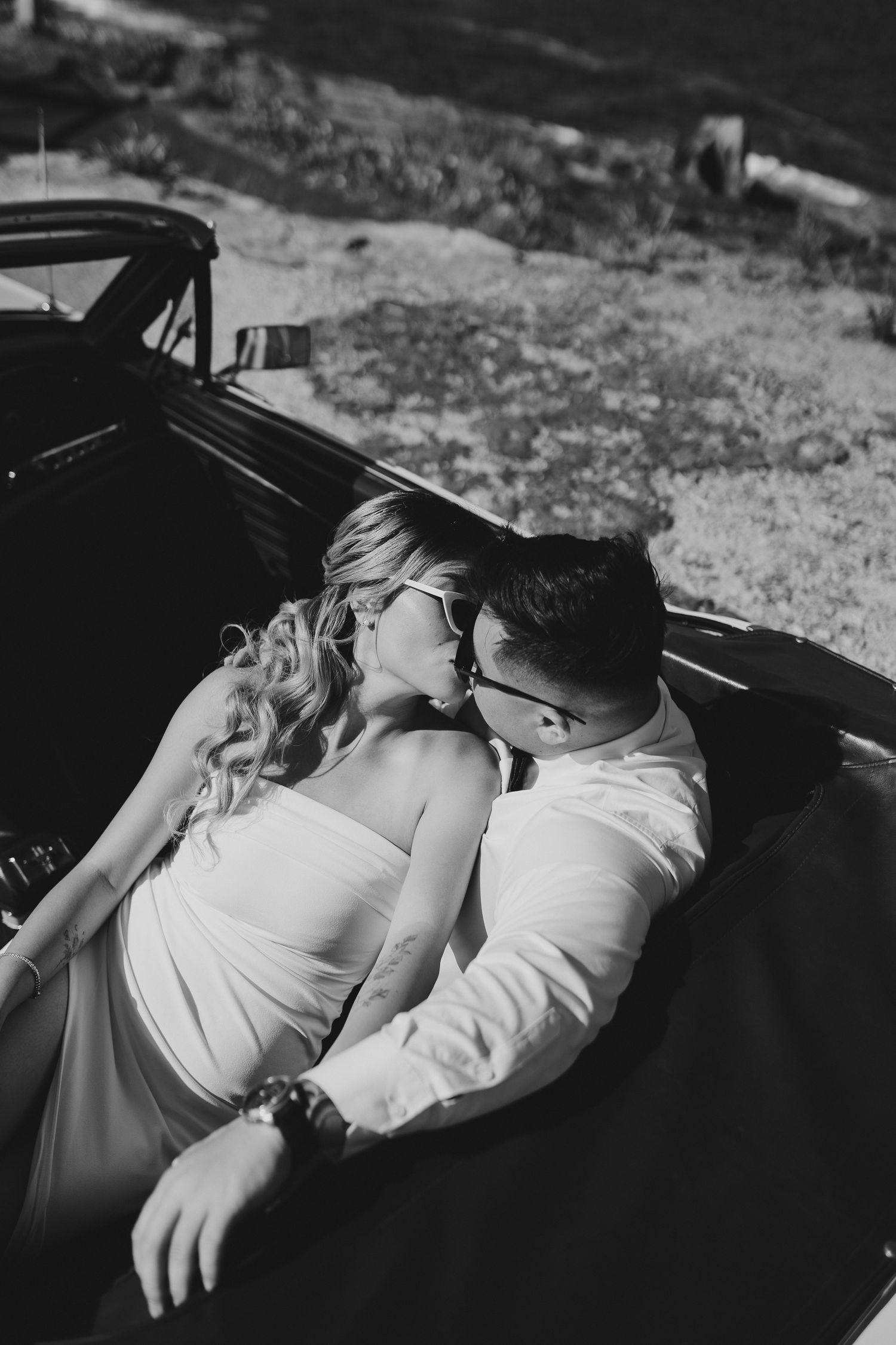 Intimate black and white portrait of a couple in a classic car by the shore.