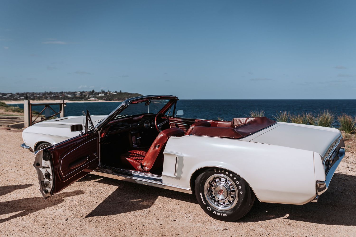 Classic white convertible car parked on coastal cliff overlooking ocean view.
