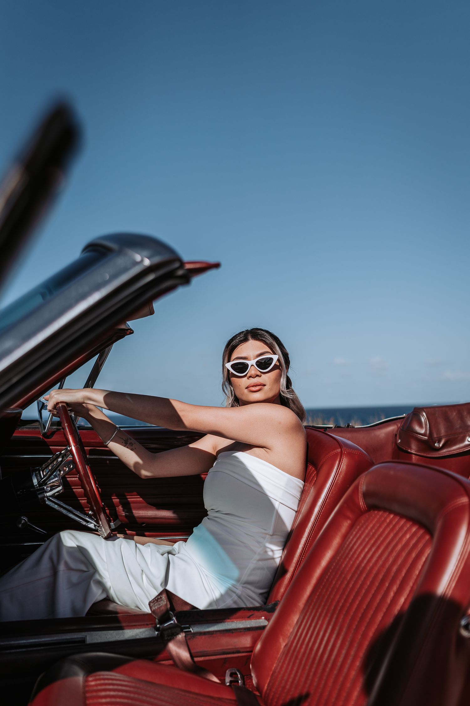 Vintage convertible car with red leather interior parked by oceanside cliff.