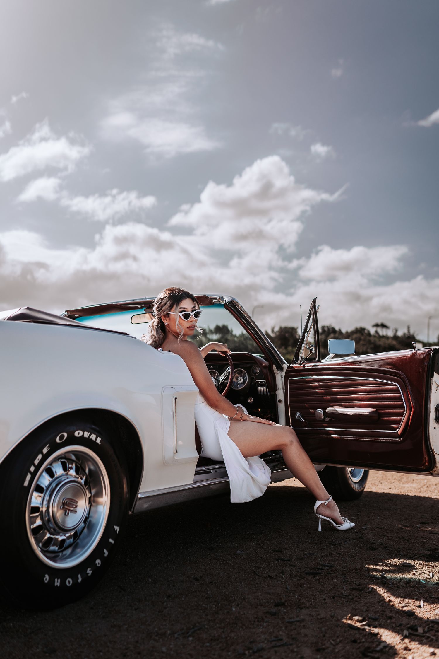Stylish classic car photoshoot featuring white vintage convertible against cloudy sky.