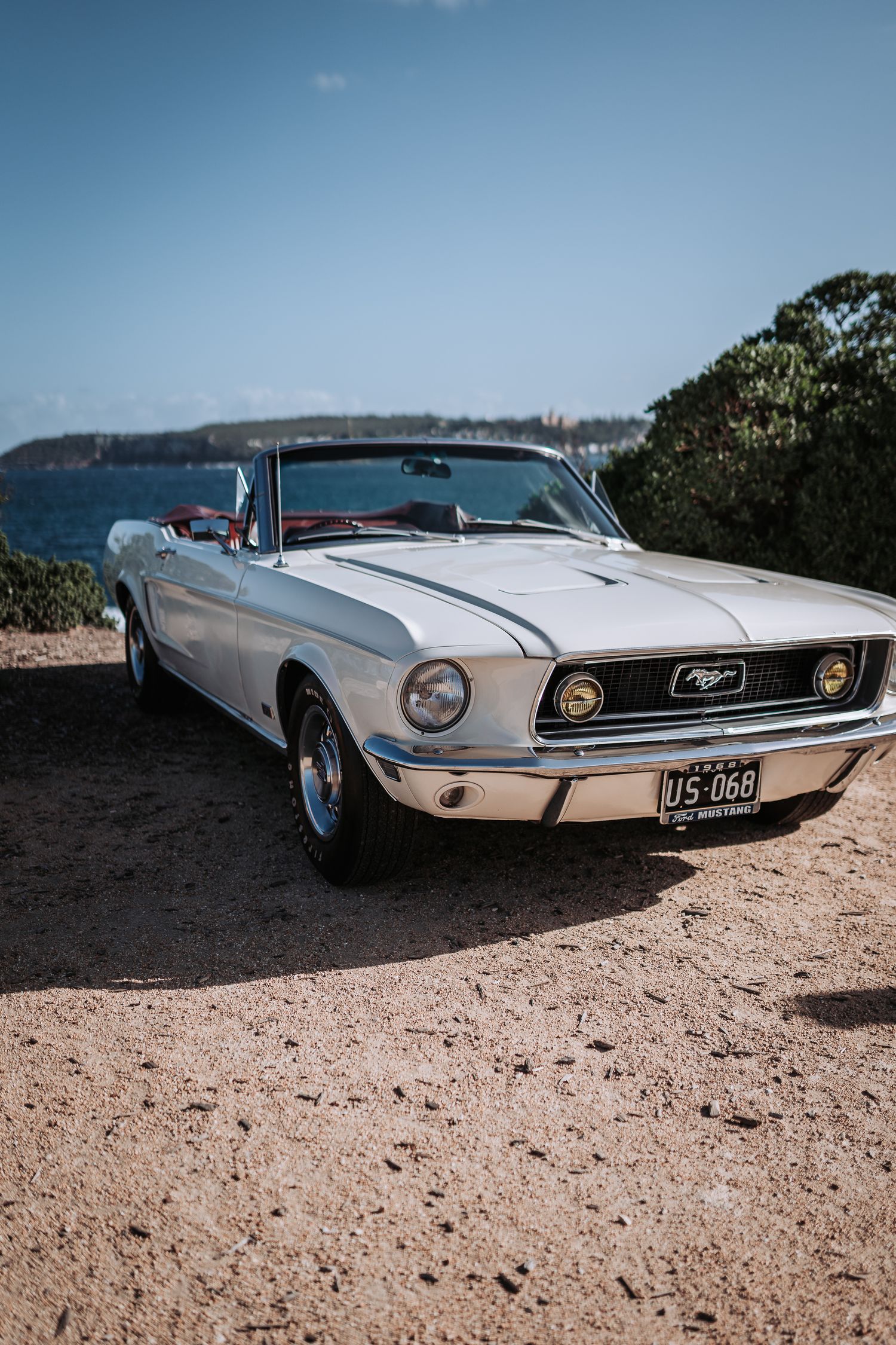 Classic white Ford Mustang convertible parked on coastal cliff overlooking ocean view.