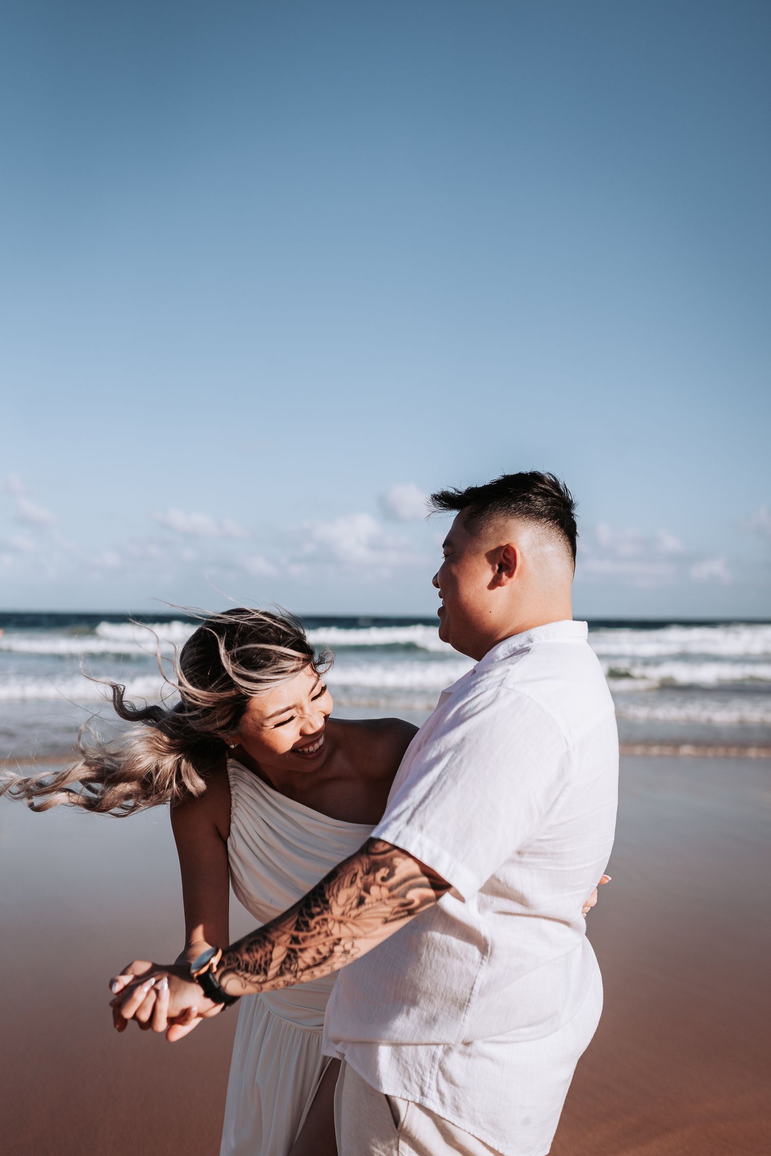 A romantic beach dance captured in motion against ocean waves and blue sky.