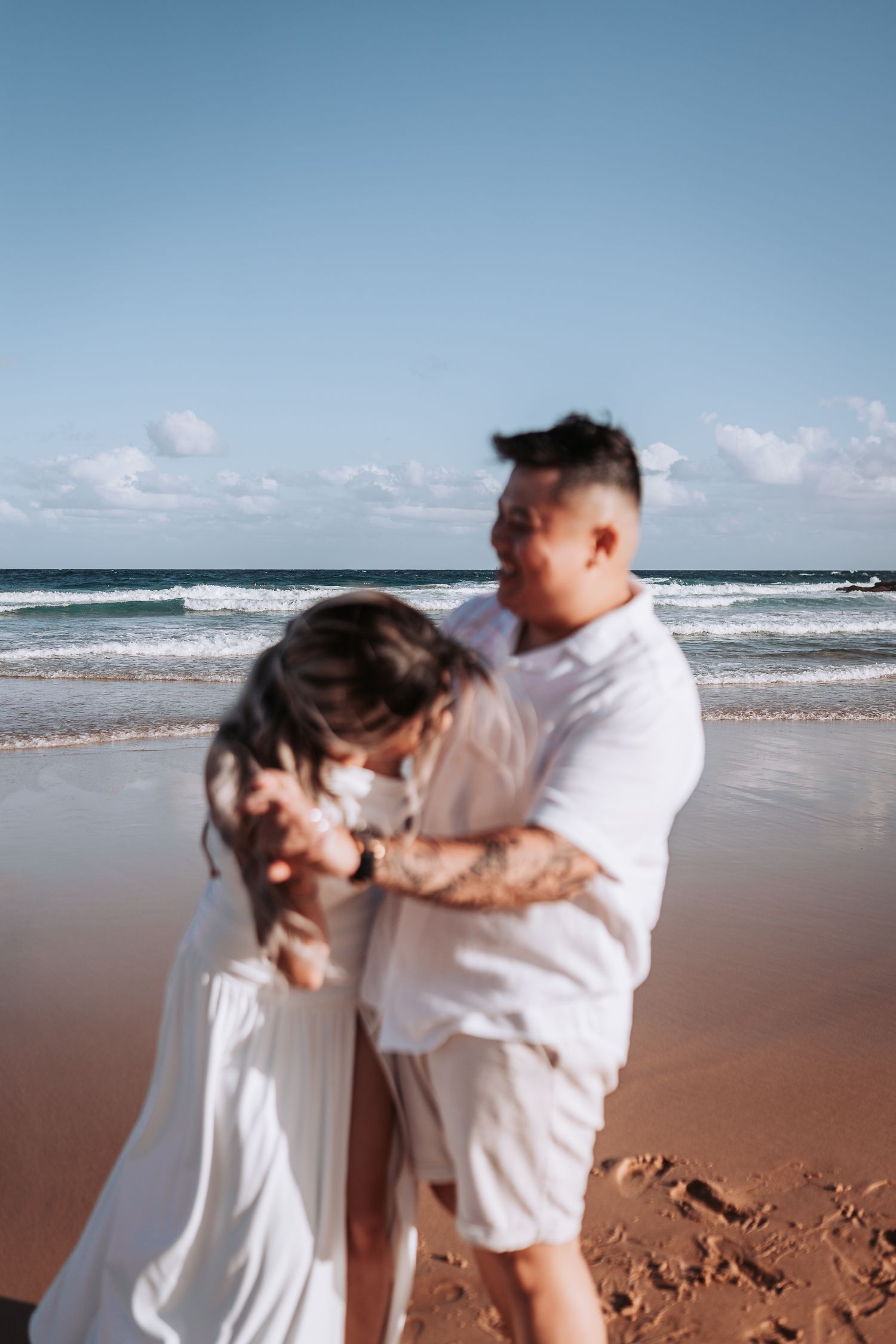 Joyful moment between couple playing on sandy beach with ocean waves behind them.