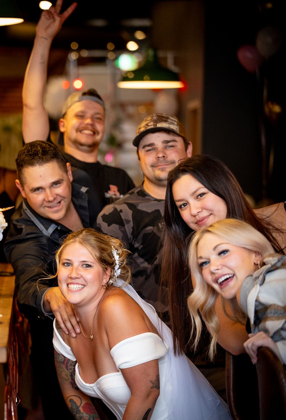 Joyful bride in white dress celebrating with tattooed friends and guests at a wedding reception.