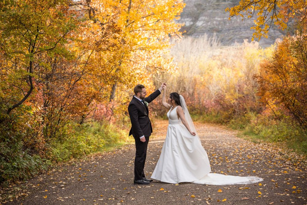 Bride and groom celebrate on a path surrounded by golden autumn leaves.