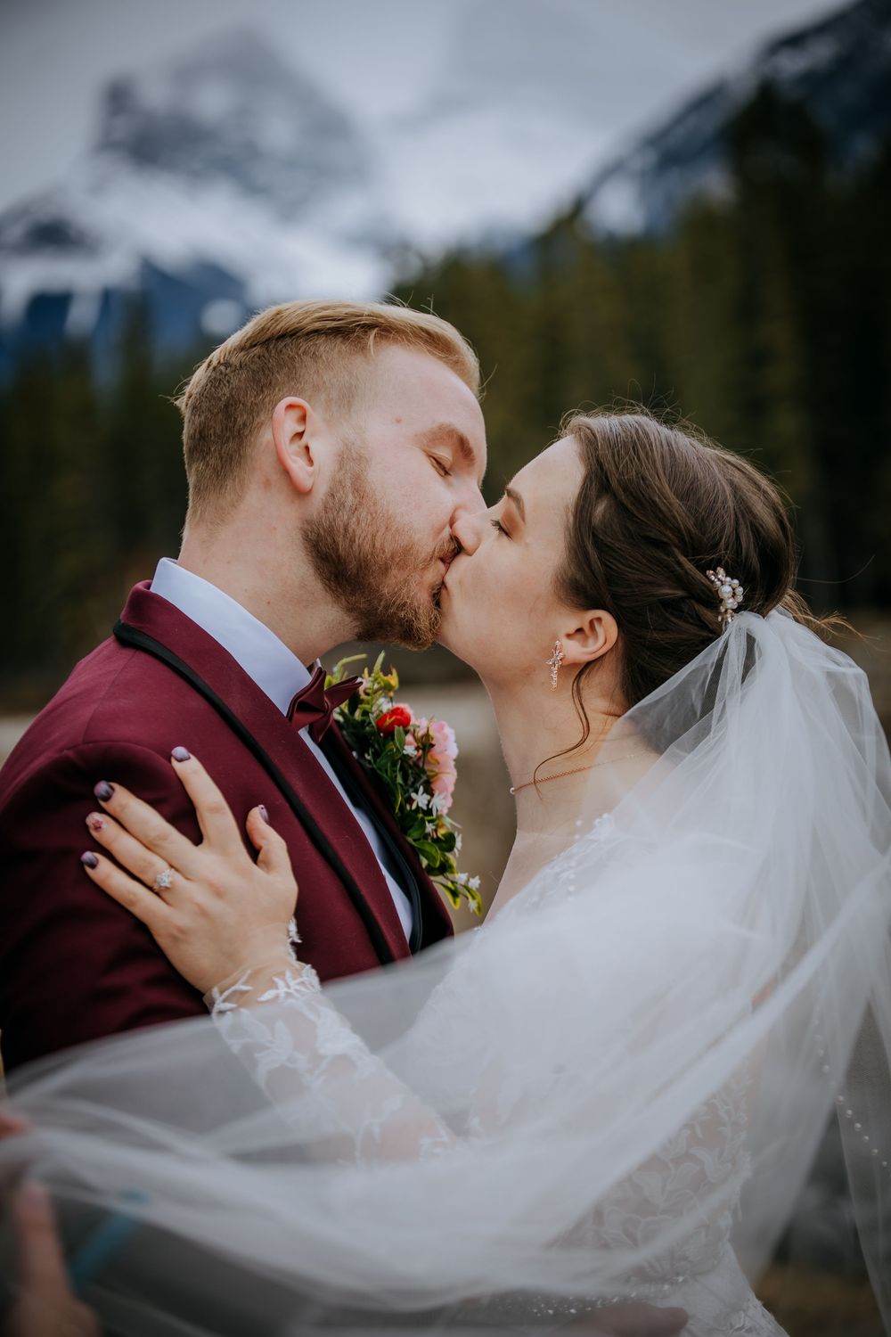 Bride and groom kissing passionately as her veil flows in the wind with misty mountains in the background.