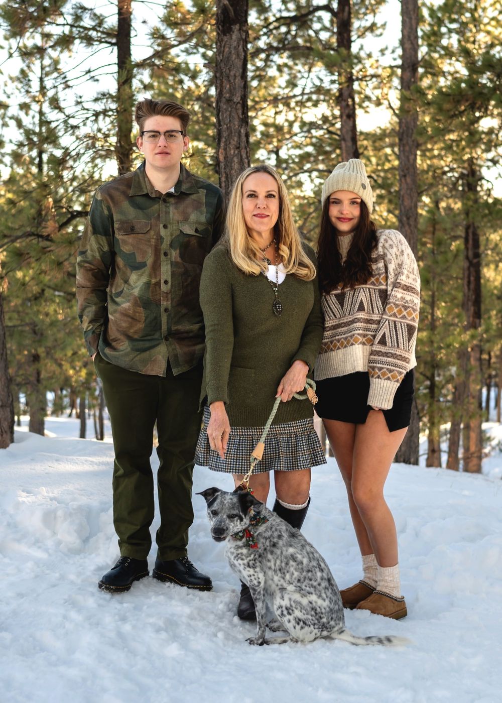 Group portrait in winter forest with dog on snowy ground among pine trees.