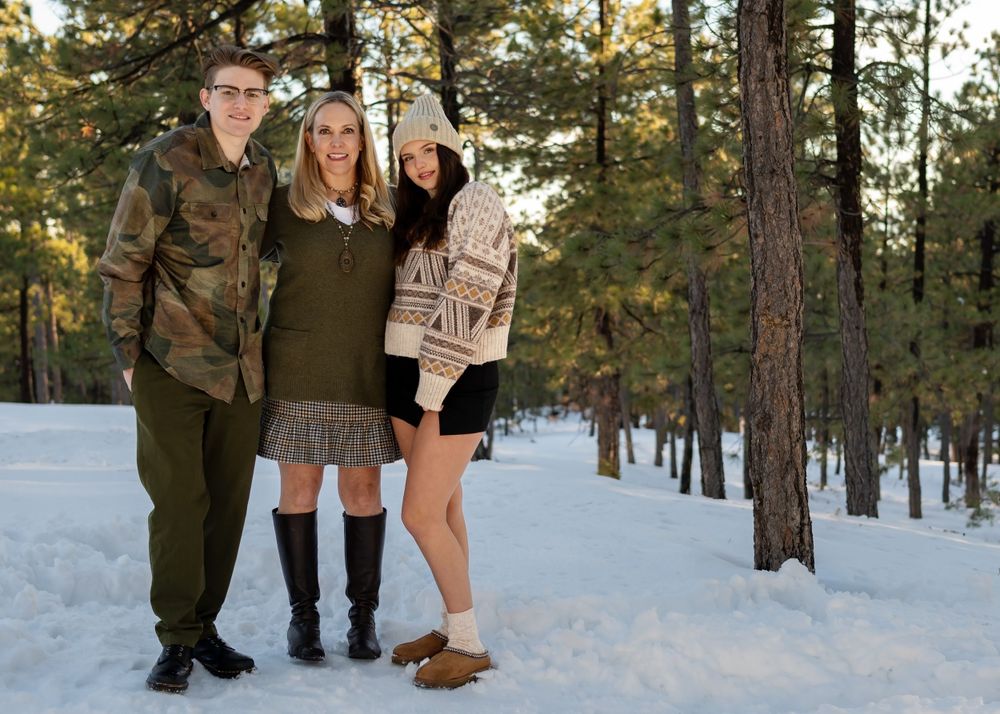 Group photo in snowy pine forest with people wearing winter clothing.