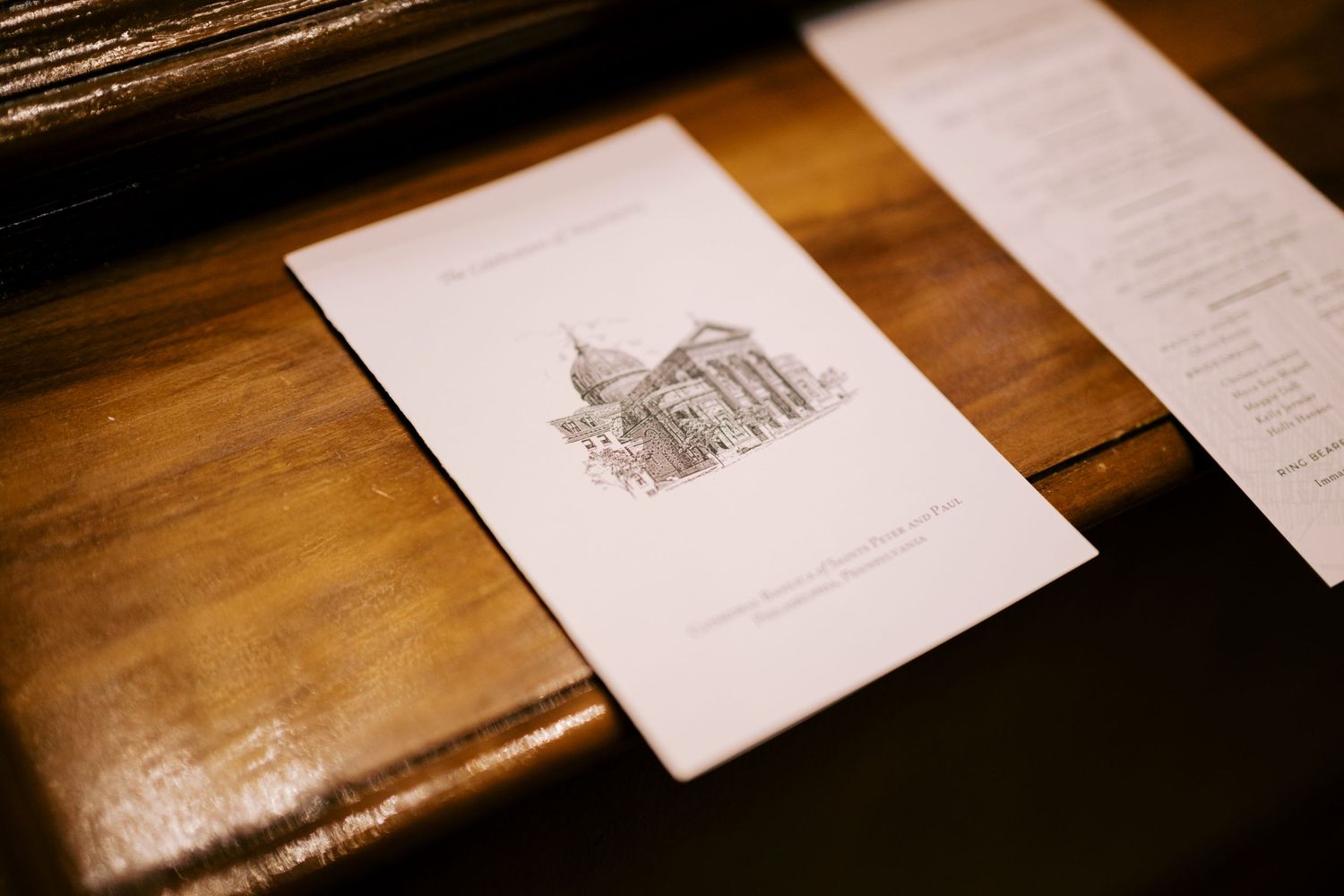 A delicate pencil sketch of a church building lies on a wooden surface beside papers in warm lighting.