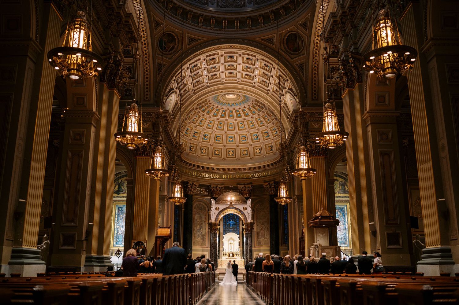 Interior view of an ornate cathedral with hanging chandeliers and a domed ceiling with intricate patterns and arches.