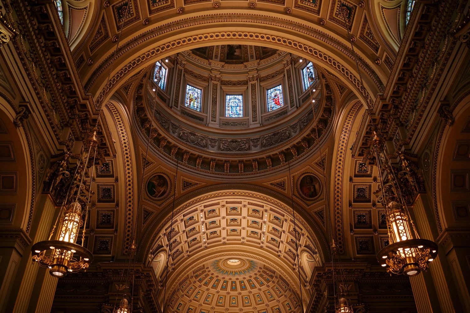 Cathedral dome interior featuring intricate baroque architecture with stained glass windows and decorative gold moldings.