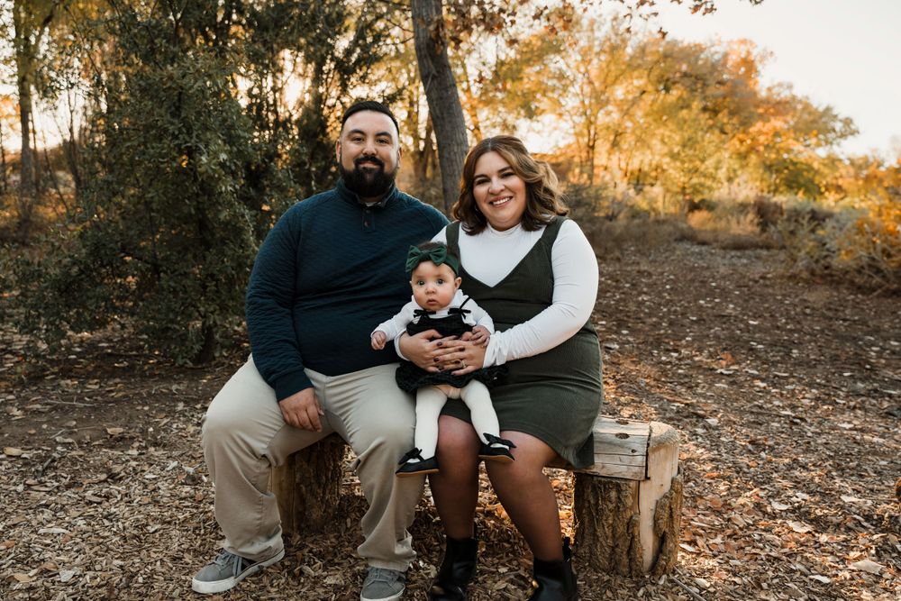 Family sitting together on wooden stumps during an outdoor autumn photo session.