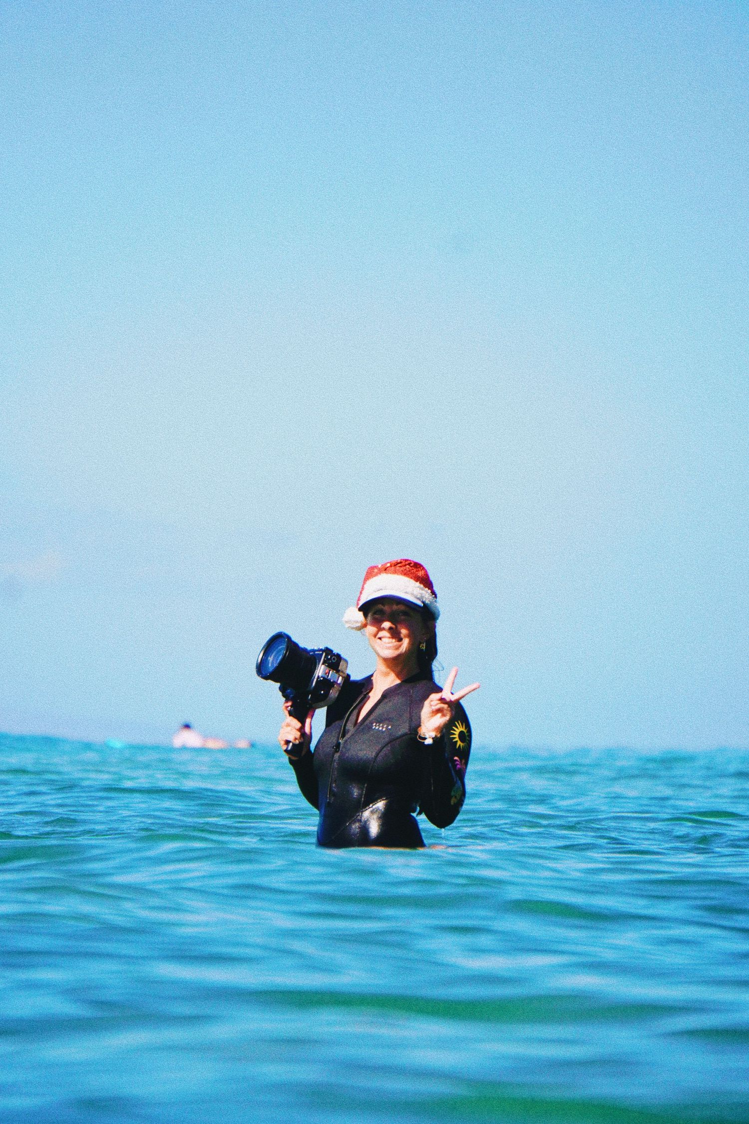 A person in a Santa hat floats in bright blue ocean water. surf photography maui hawaii