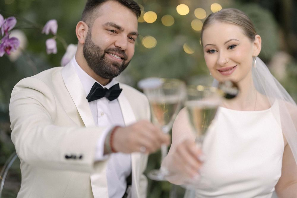 A couple in wedding attire toasts with champagne glasses during an outdoor celebration.