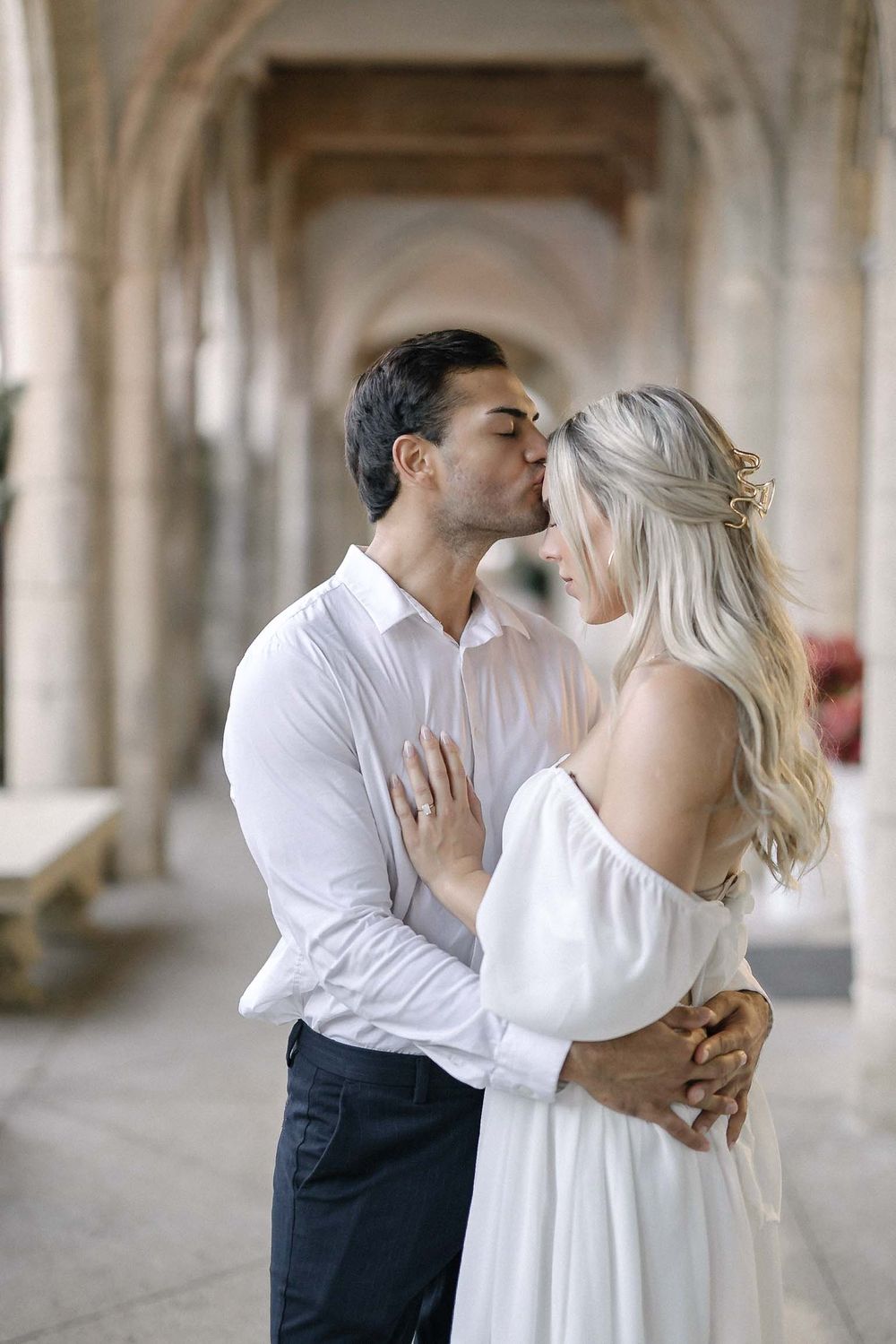 A romantic moment in an elegant archway corridor as a couple shares a tender kiss.