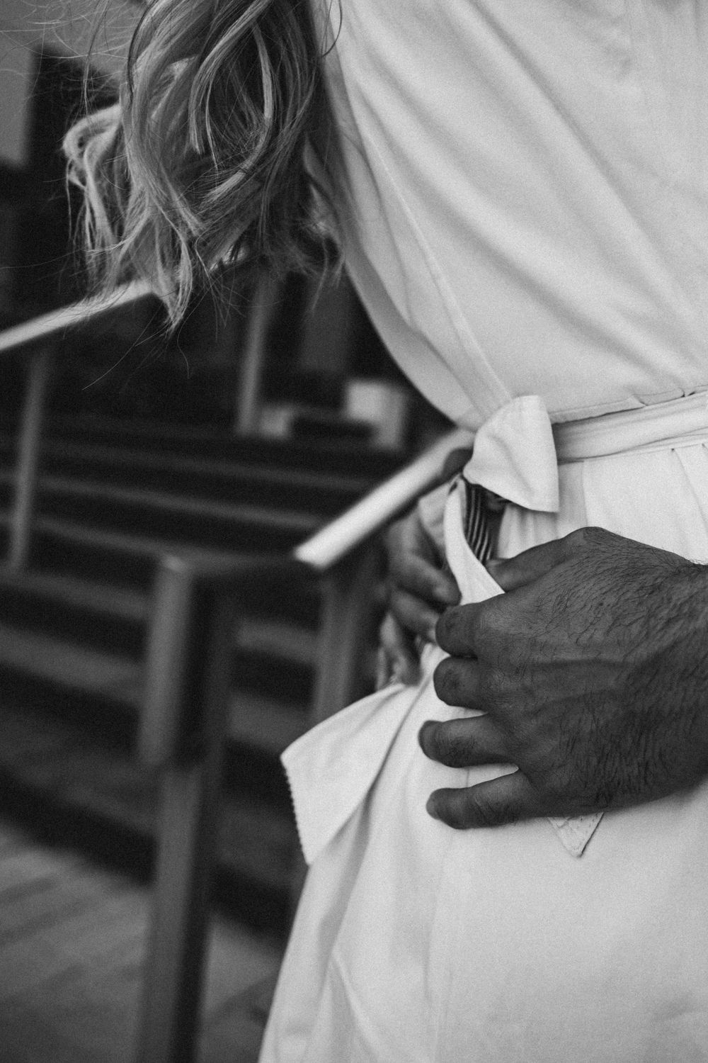 Black and white close-up of an intimate embrace showing hands holding a white dress.