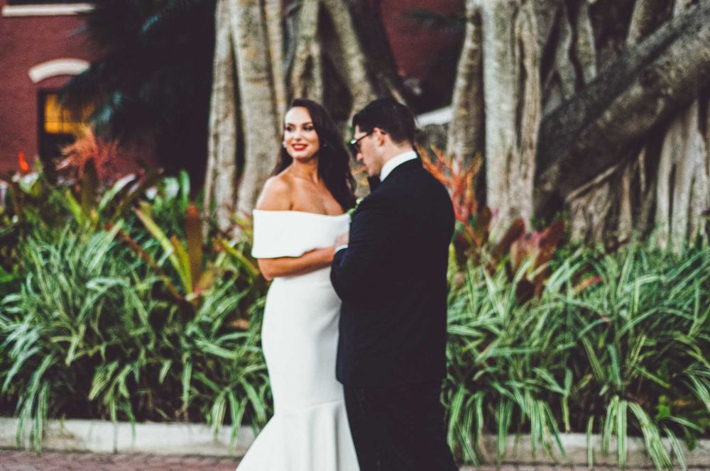 A wedding couple sharing an intimate moment in front of lush tropical foliage.