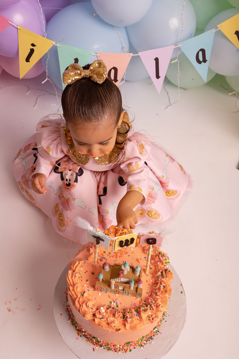 Birthday cake decorated with sprinkles and castle topper under colorful balloon garland.