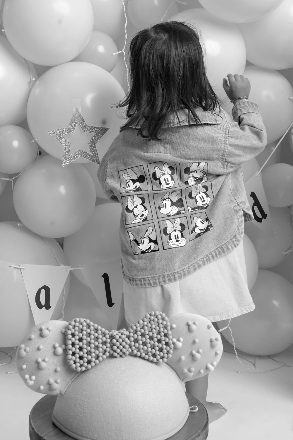 A denim jacket with Mickey Mouse patches against a backdrop of white and silver balloons.
