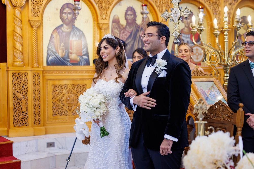 Bride holding white bouquet and groom in tuxedo smiling after Orthodox Christian wedding ceremony in church.