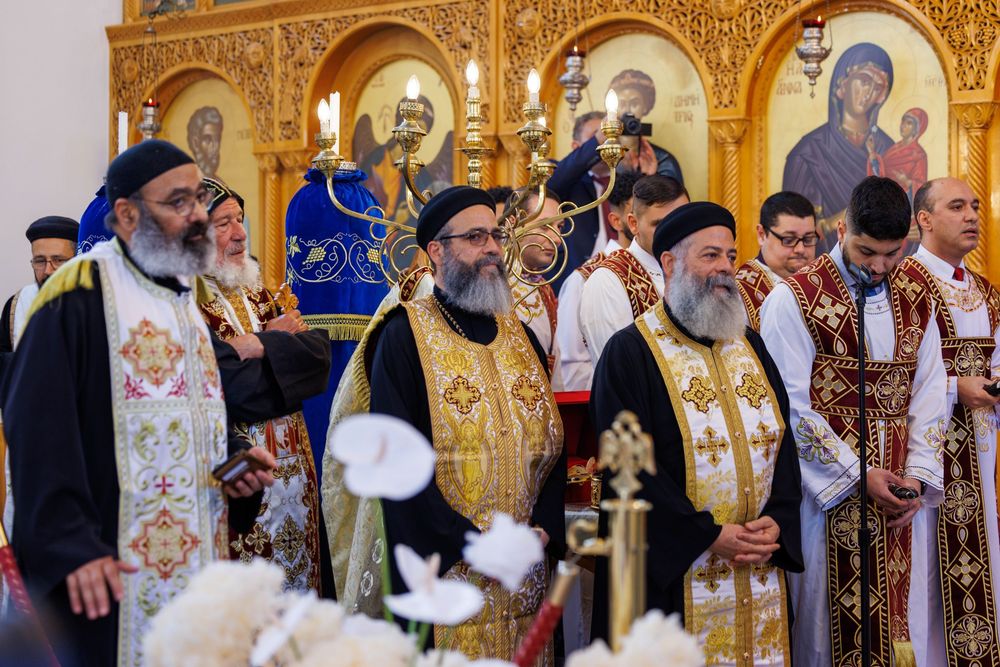 Procession of Coptic Orthodox priests in ceremonial vestments during religious service at decorated church.