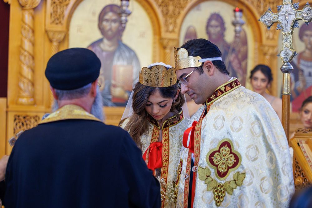 Couple bows during Coptic Orthodox wedding ceremony with priest and golden iconostasis.