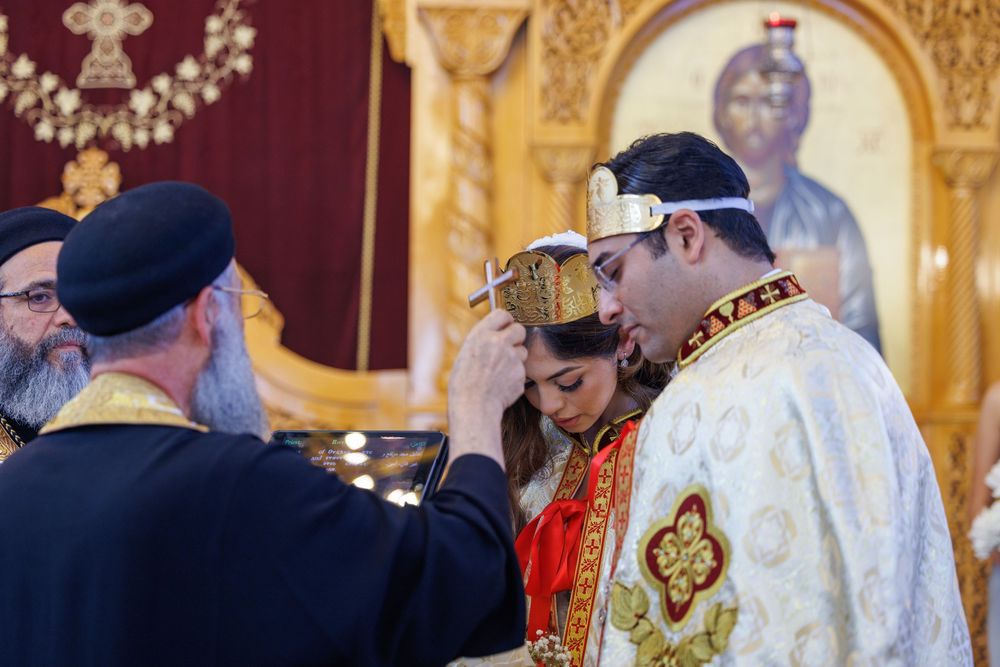 Priest places crown on groom during Coptic Orthodox wedding crowning ceremony in church.