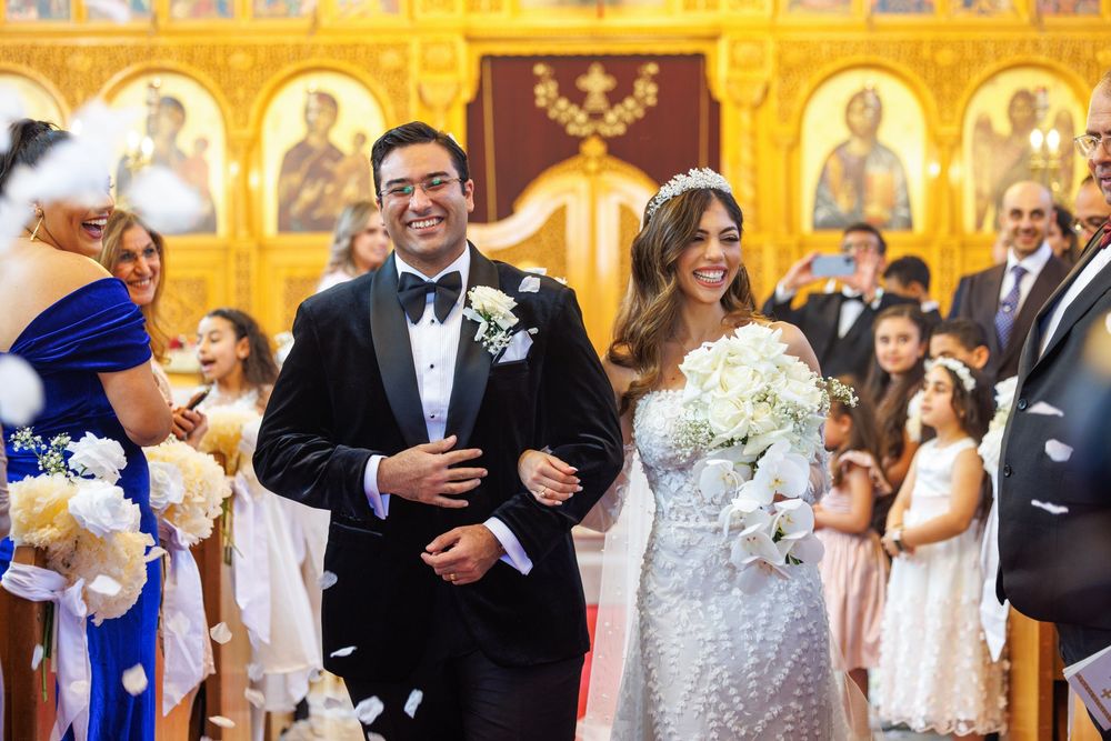 Newlyweds walk down aisle after Coptic Orthodox wedding ceremony surrounded by guests.