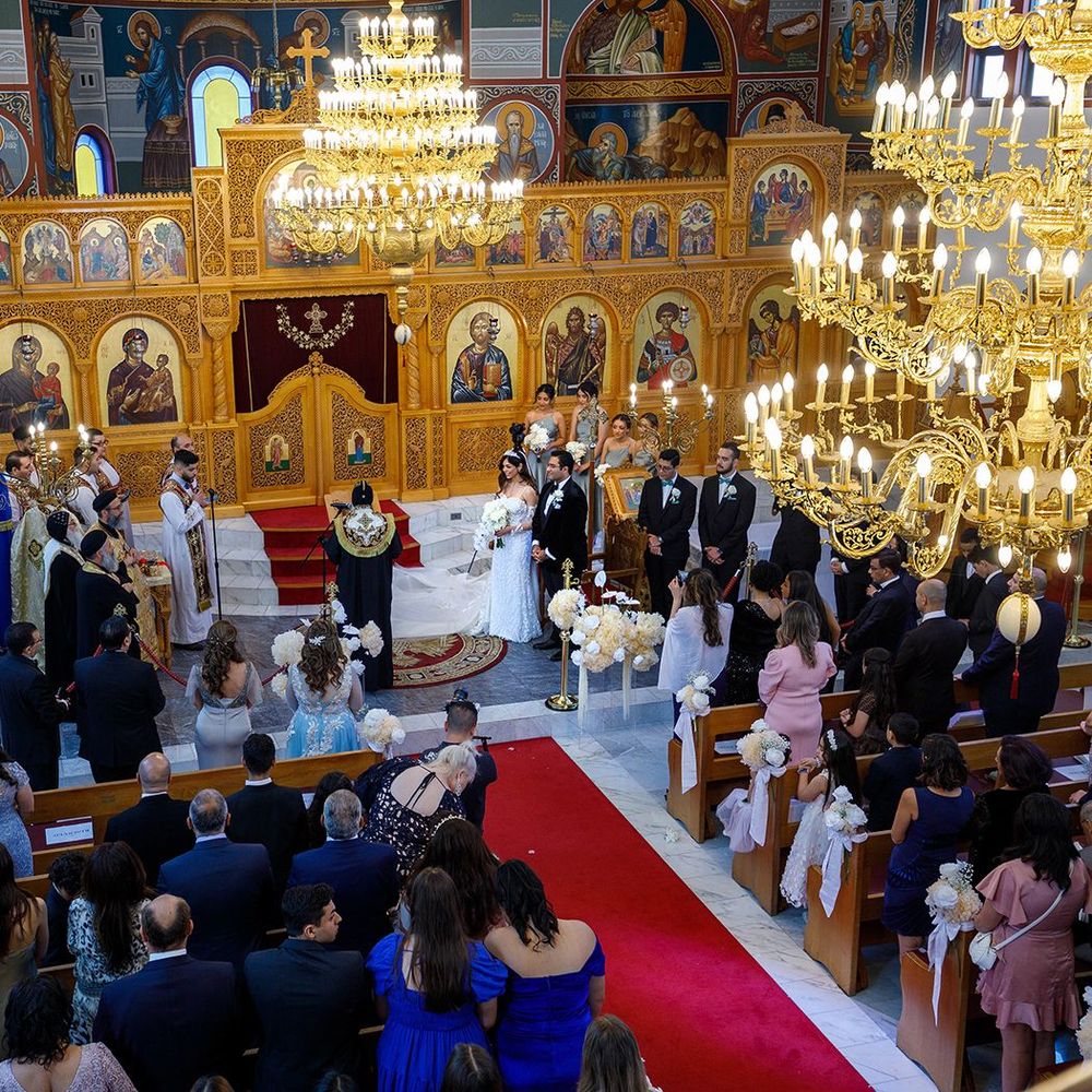 Wide view of Coptic Orthodox wedding ceremony in ornate church with chandelier and guests.