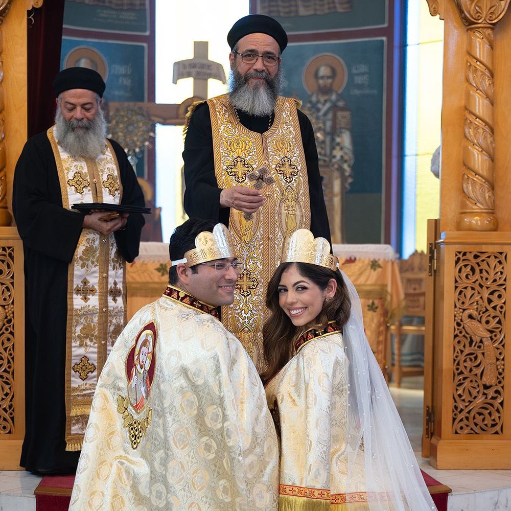 Two priests officiate Coptic Orthodox wedding with crowned bride and groom at altar.
