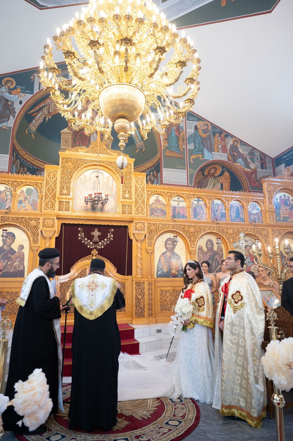 Bride and groom stand before golden iconostasis during Coptic Orthodox wedding ceremony.