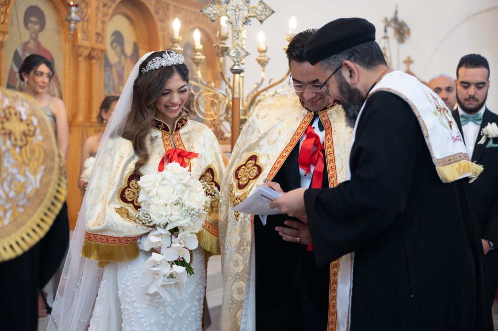 Bride and groom in ornate robes during Orthodox Christian wedding ceremony with priest reading vows.