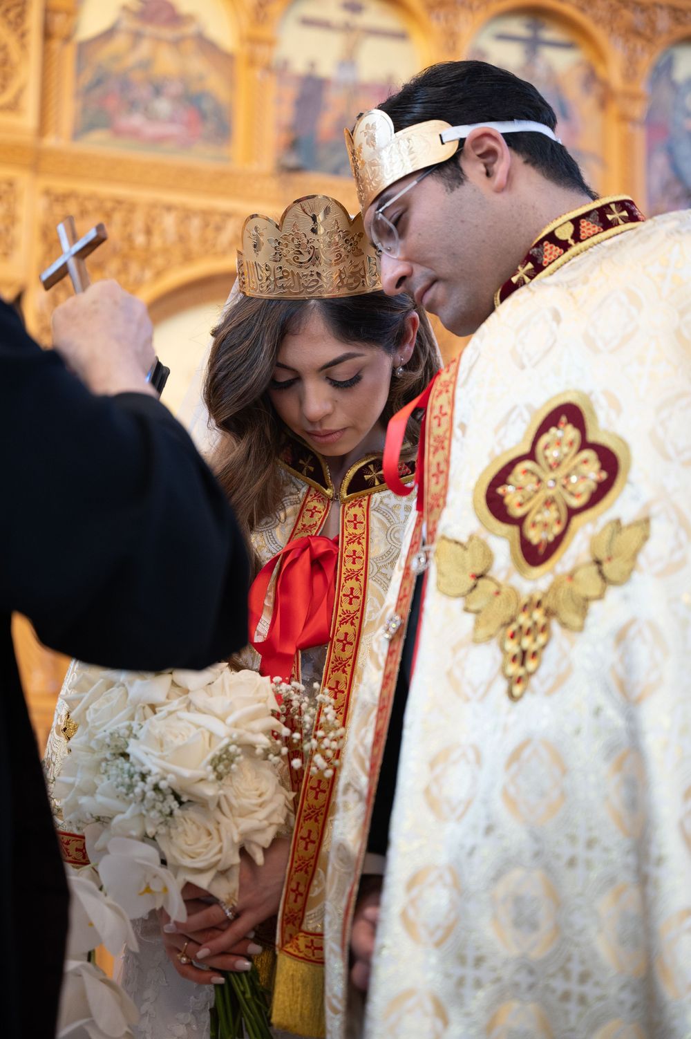 Couple wearing golden crowns in traditional Orthodox wedding ceremony with decorated church interior.