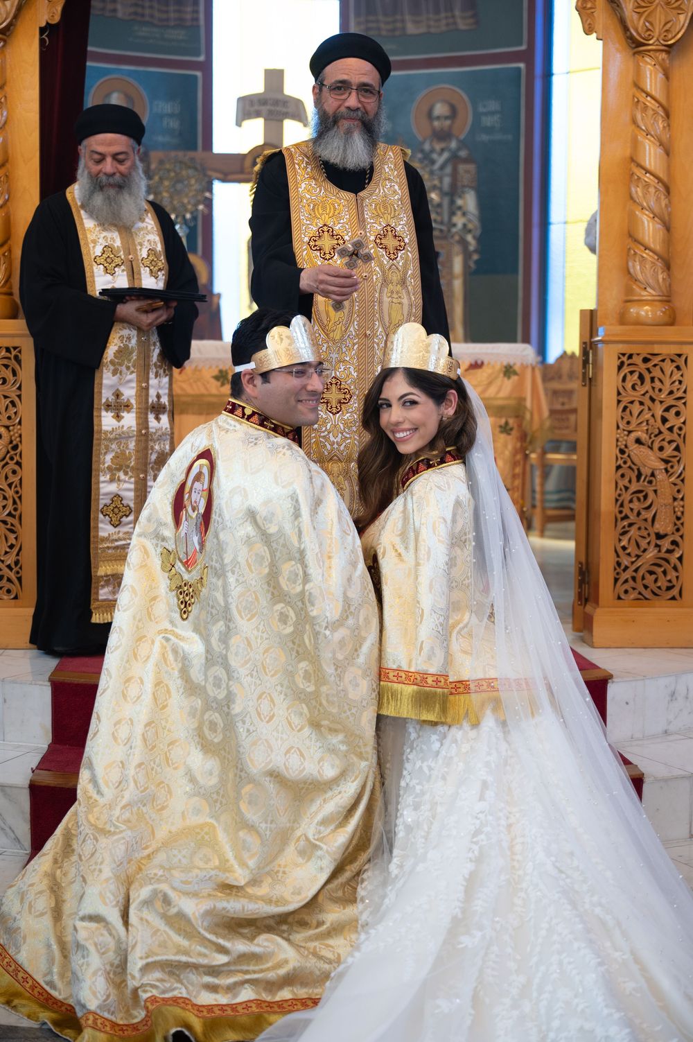 Newlyweds in matching gold embroidered robes pose with Orthodox priests after wedding ceremony.