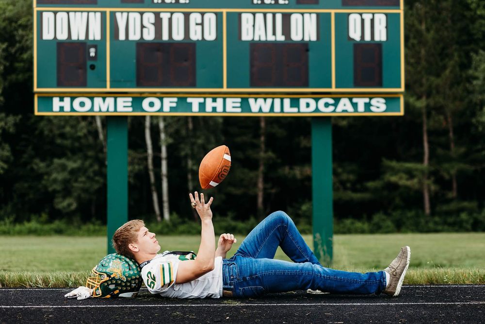 Person lying on track with football under scoreboard reading Home of the Wildcats.