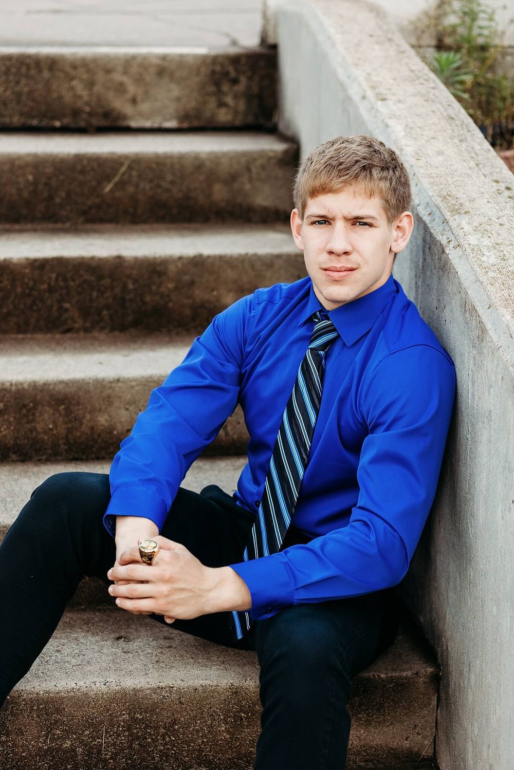 Professional portrait of person in blue dress shirt and striped tie sitting on concrete steps.