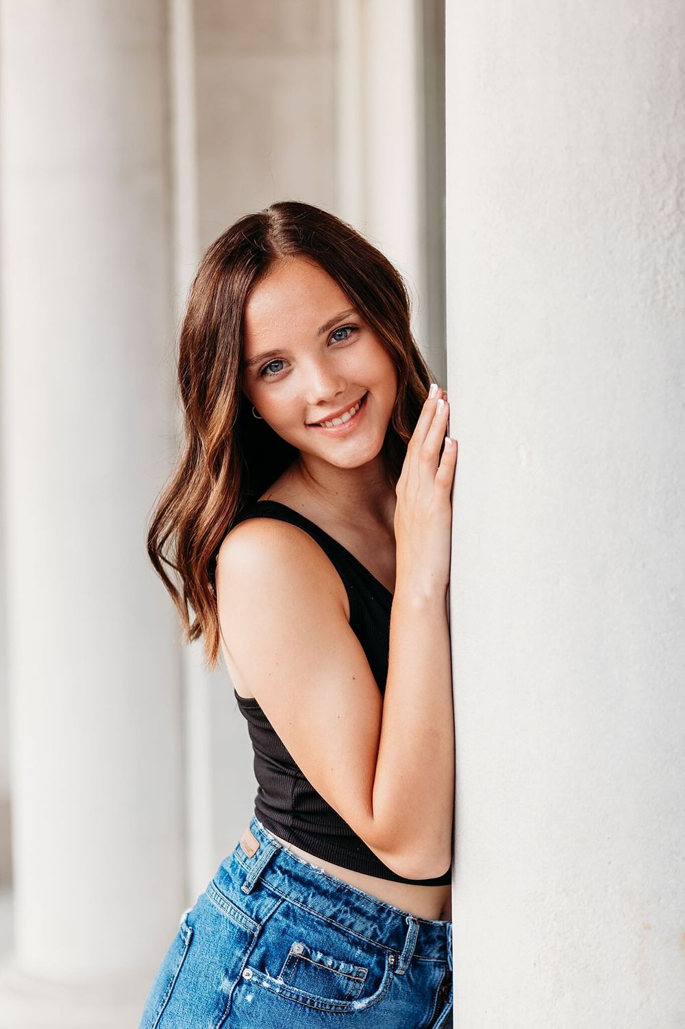 Casual portrait against white wall wearing black tank top and denim.