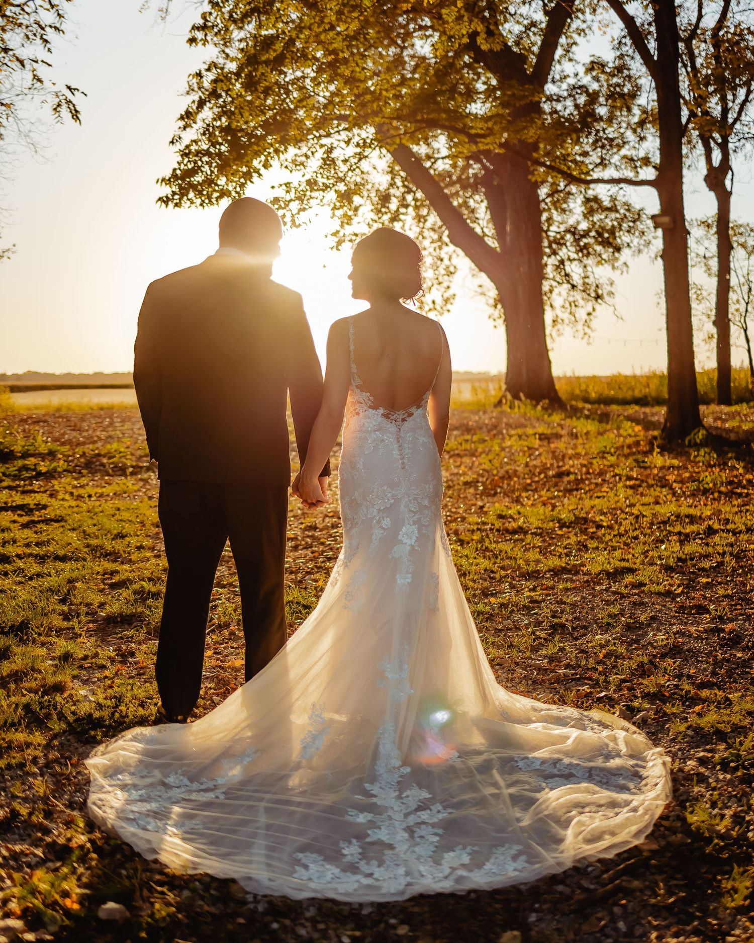 Silhouette of newlyweds at sunset with long train wedding dress and autumn trees.