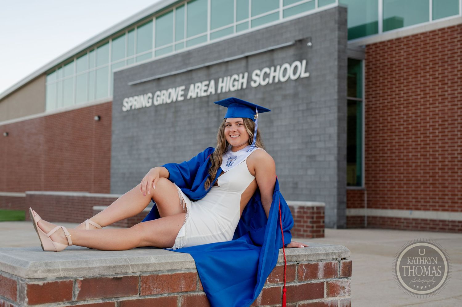Graduate in blue cap and gown poses in front of Spring Grove Area High School sign.