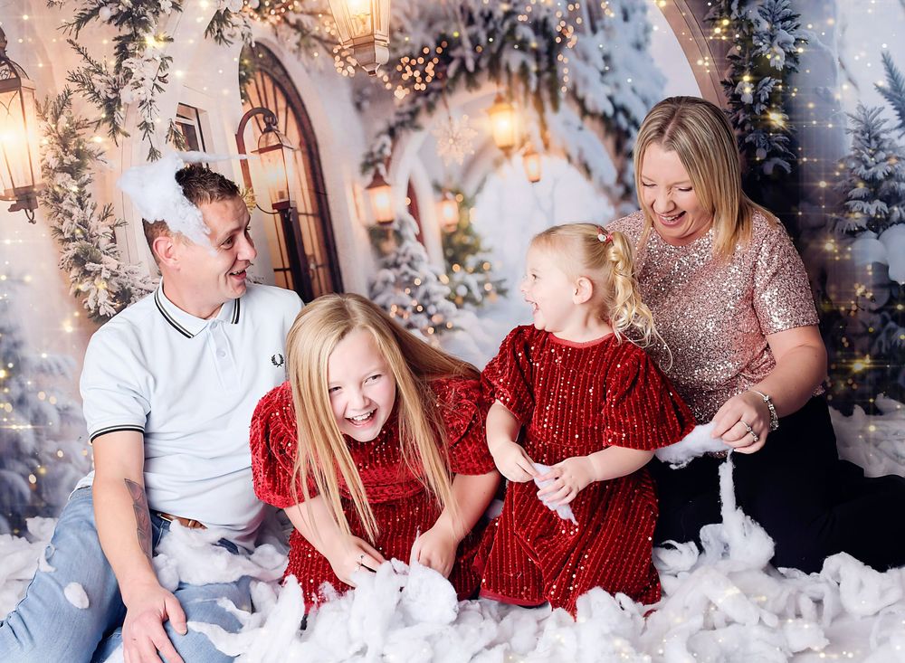 Christmas family photography by Nicola in Woodside, capturing family laughing in falling snow, joyful festive portrait full of warmth