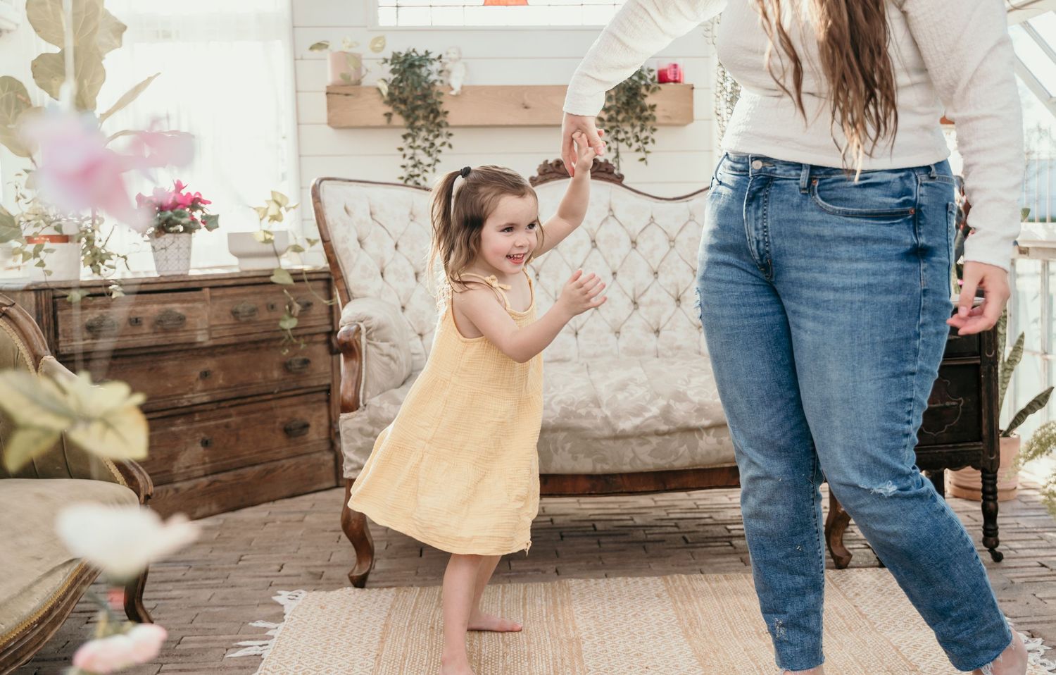 A small child in a yellow dress dances joyfully in a rustic indoor setting.