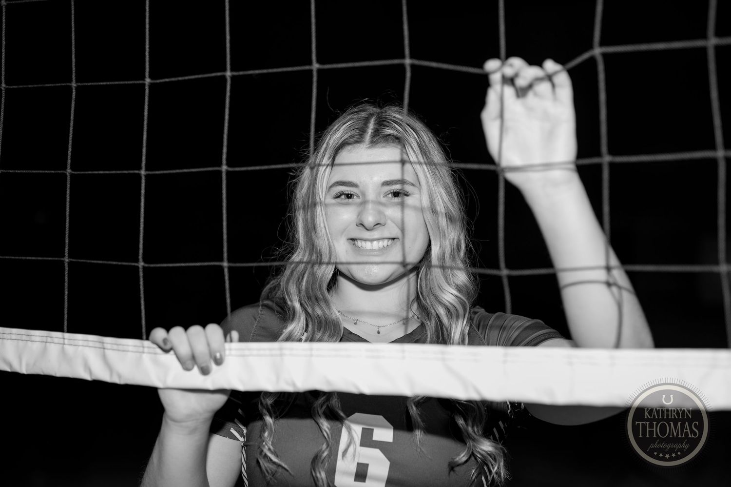 Black and white portrait of volleyball player holding net in indoor gymnasium.