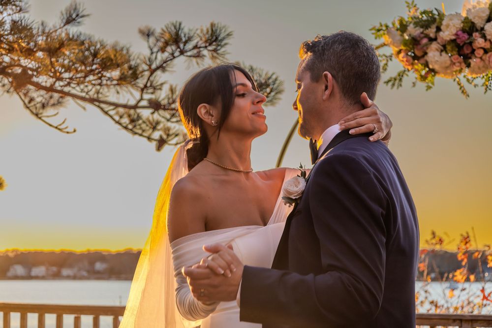A bride and groom share an intimate moment at sunset on a waterfront balcony with golden light illuminating the scene.