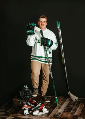 Hockey player poses with equipment including stick, gloves, skates and helmet on wooden platform.