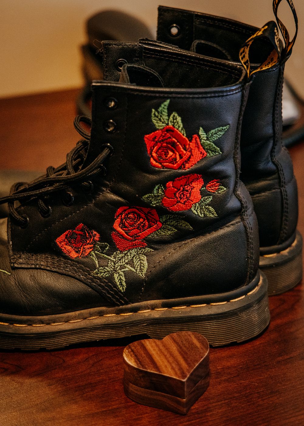Black leather boots with embroidered red roses sit on a wooden surface in varying close-up shots.