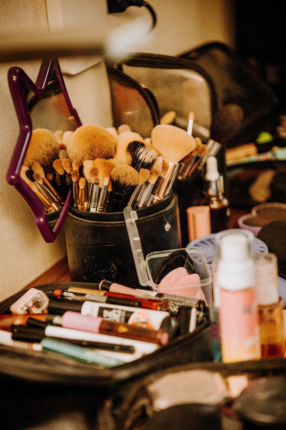 Makeup brushes and cosmetic products arranged on a vanity table with soft warm lighting.